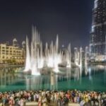 A crowd of people standing around a fountain with The Dubai Fountain in the background Description automatically generated