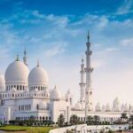 A large white building with domes and towers with Sheikh Zayed Mosque in the background Description automatically generated