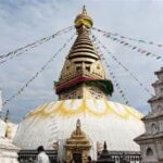 A temple with flags from the roof with Swayambhunath in the background Description automatically generated with medium confidence