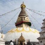 A temple with flags from the roof with Swayambhunath in the background Description automatically generated with medium confidence