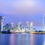 A city skyline with a ferris wheel and a body of water Description automatically generated