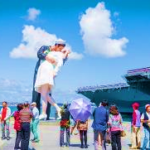 A group of people standing around a statue of a sailor kissing Description automatically generated