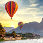 Hot air balloons flying over a river Description automatically generated